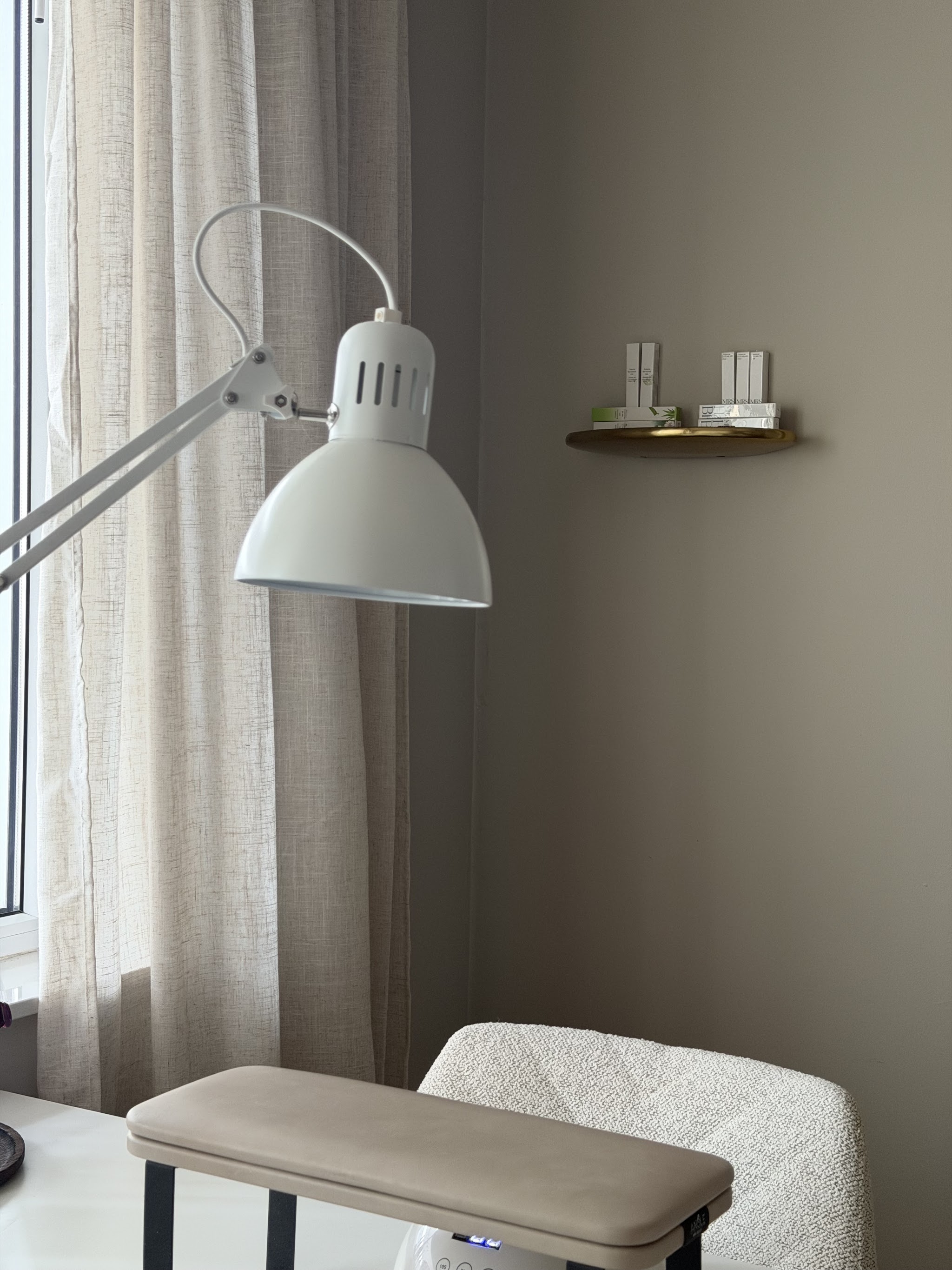 Hoek van de salon met een witte lamp, linnen gordijnen en het manicurekussen