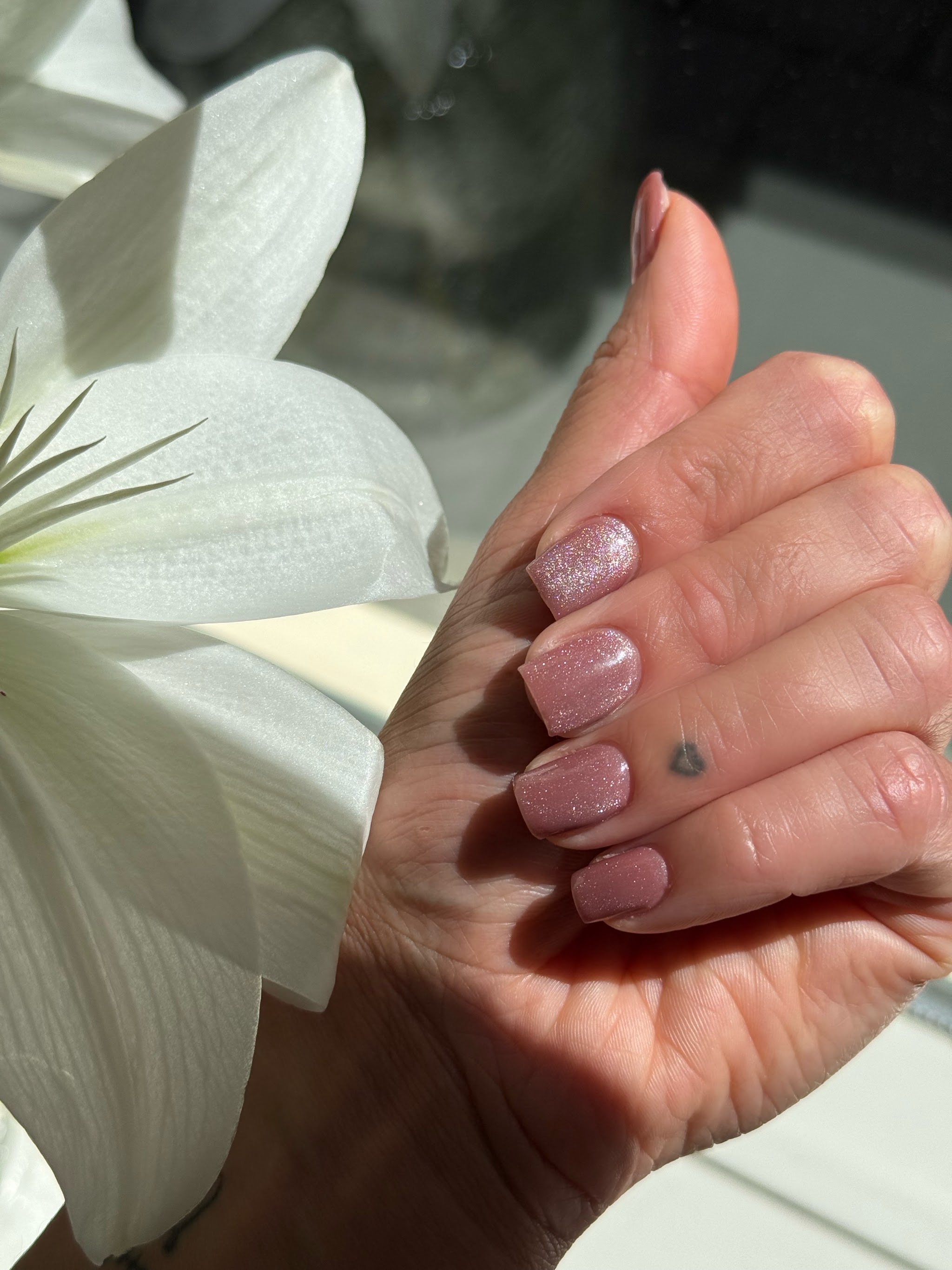 Nude nagels met glitter, naast een witte lelie