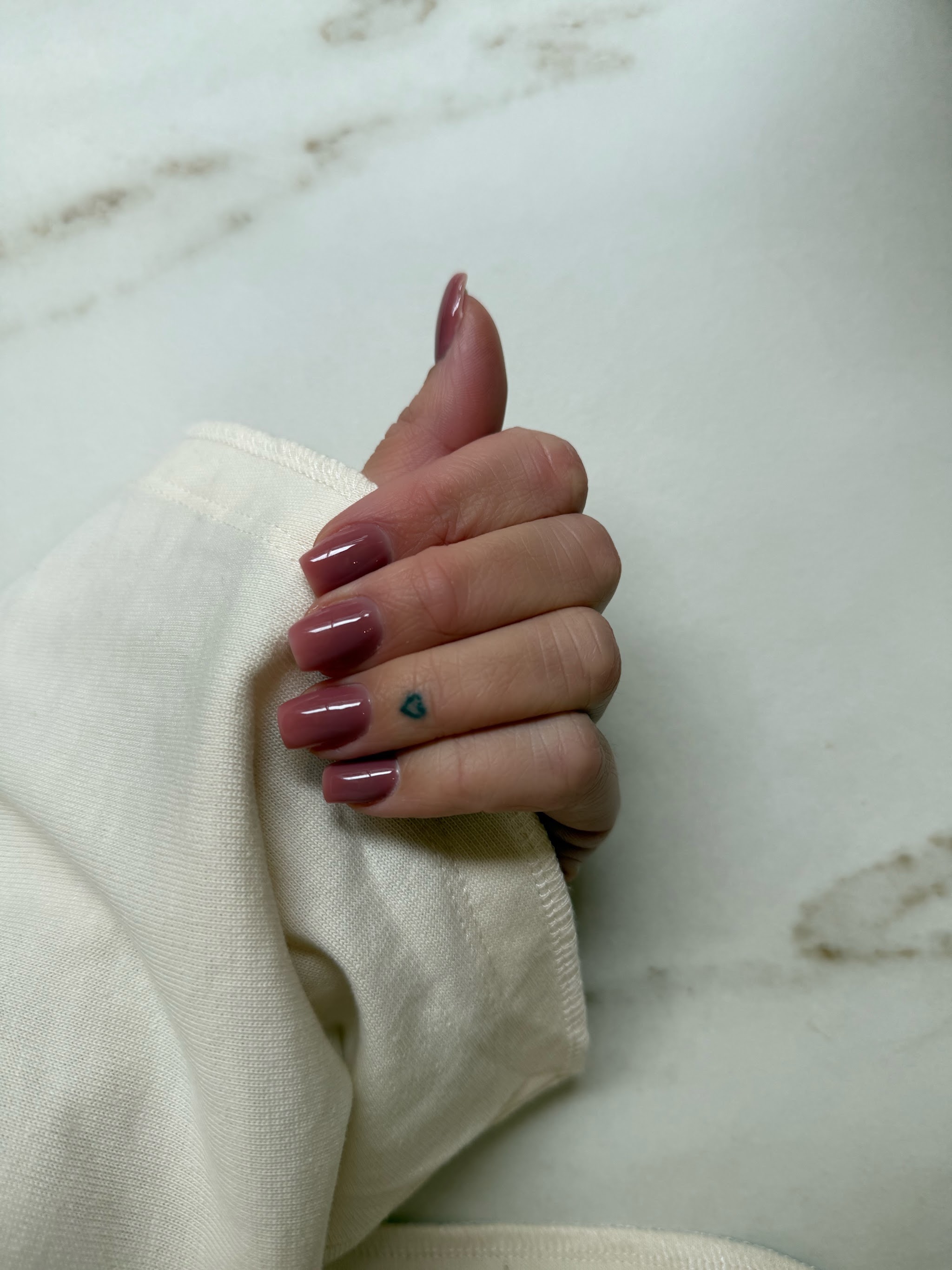 Glanzende bordeauxrode nagels op een crèmekleurige trui